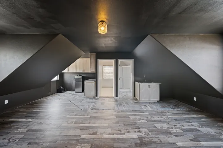 Spacious attic loft featuring peaked ceilings, abundant natural light from dormer windows, and finished wood-tone flooring throughout