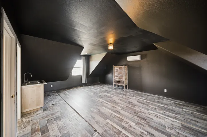 Herringbone pattern wood-finish flooring, recessed window, dark wall and ceiling finishes, built-in wet bar with stainless steel sink, and wall-mounted climate control unit