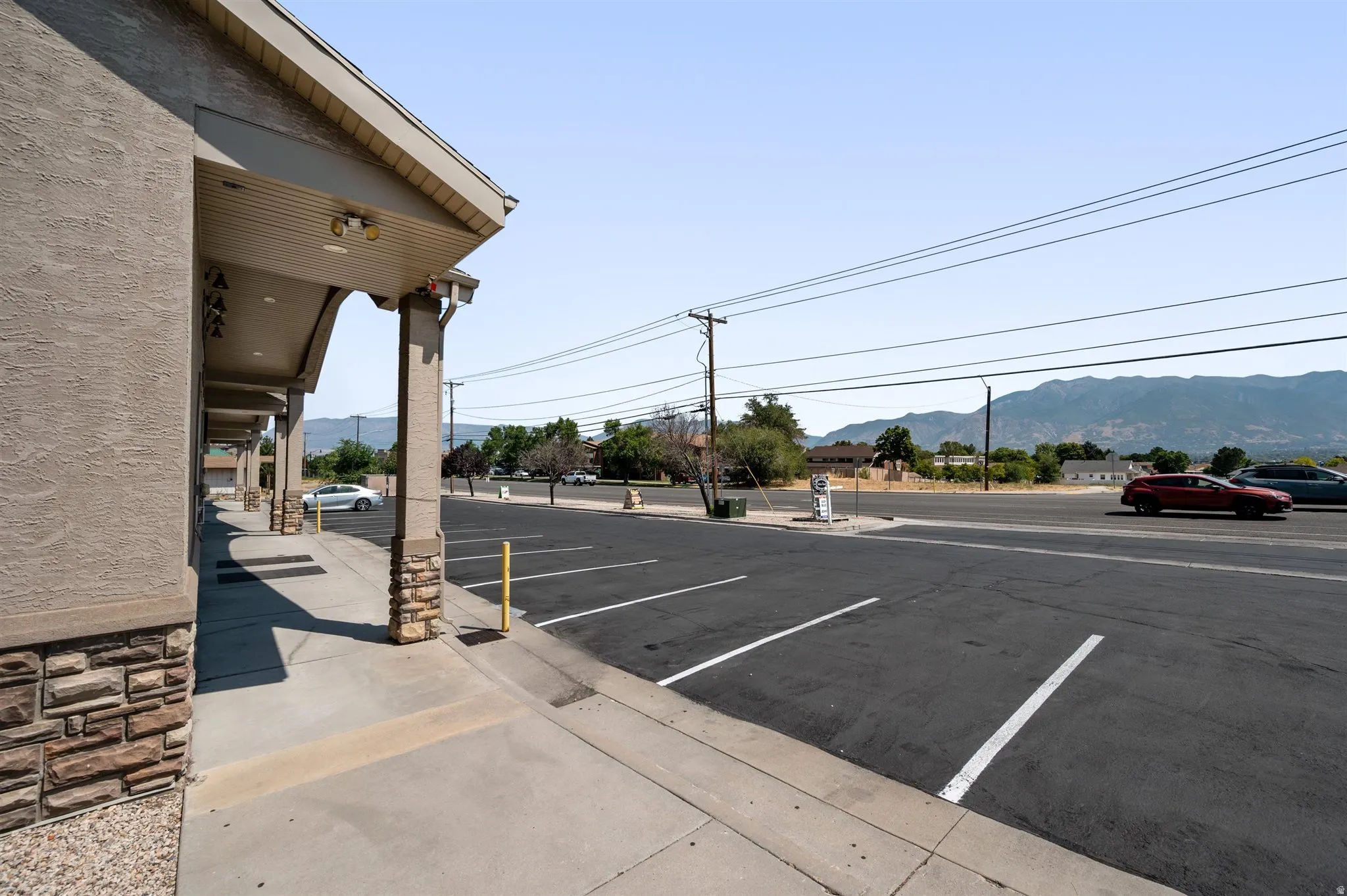 Exterior featuring stucco siding, stone veneer accents, an overhang with recessed lighting, and a paved parking area with striping