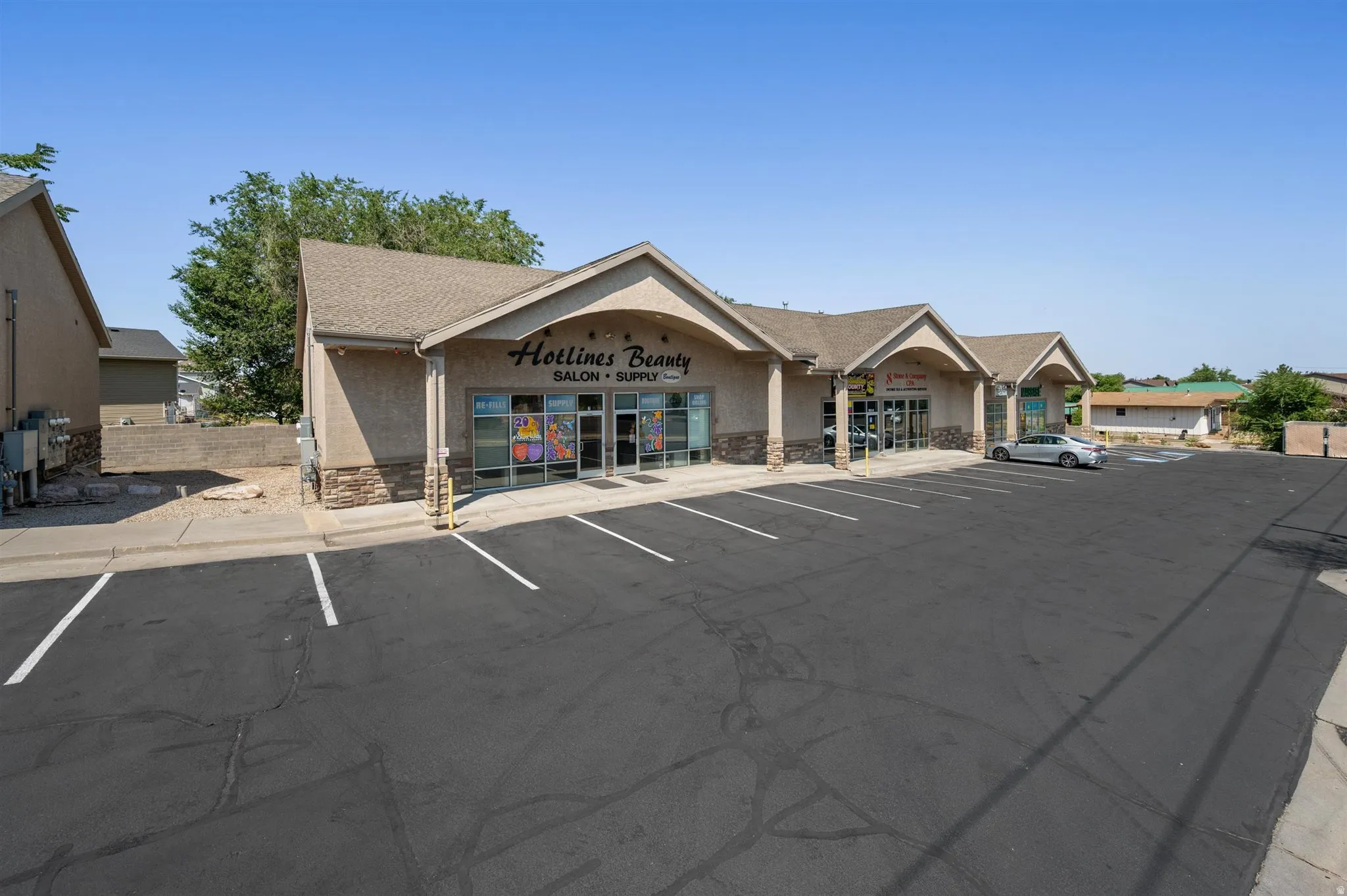 Strip mall with multiple storefronts, stucco exterior with stone accents, gable rooflines, and a large paved parking lot with marked spaces