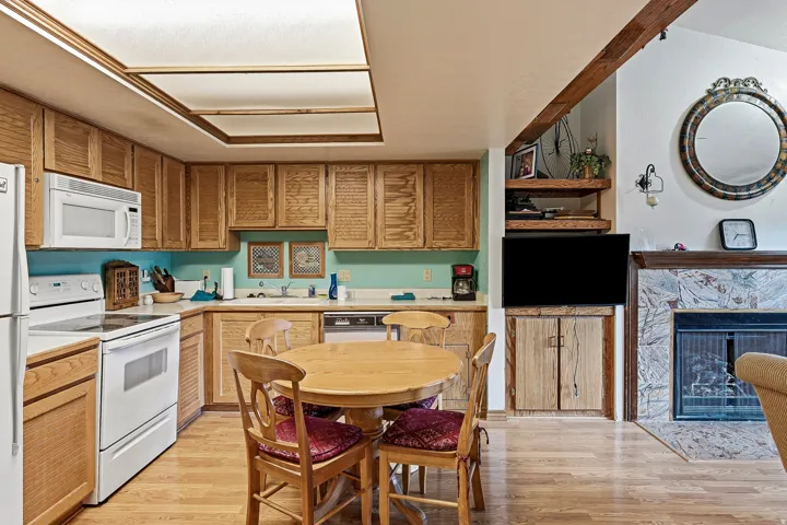 Warm wood cabinetry and solid wood flooring throughout this open-concept kitchen and dining area, featuring white appliances, turquoise tile backsplash, skylight ceiling, and a round wood dining table with seating for four