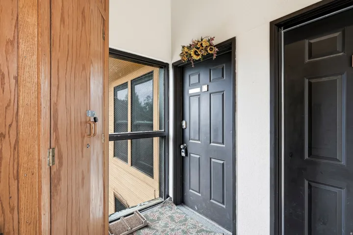 Welcoming entryway featuring a warm wood-finish exterior door, black six-panel interior door with decorative gold wreath, black-framed glass panel door with wood trim, and neutral tile flooring