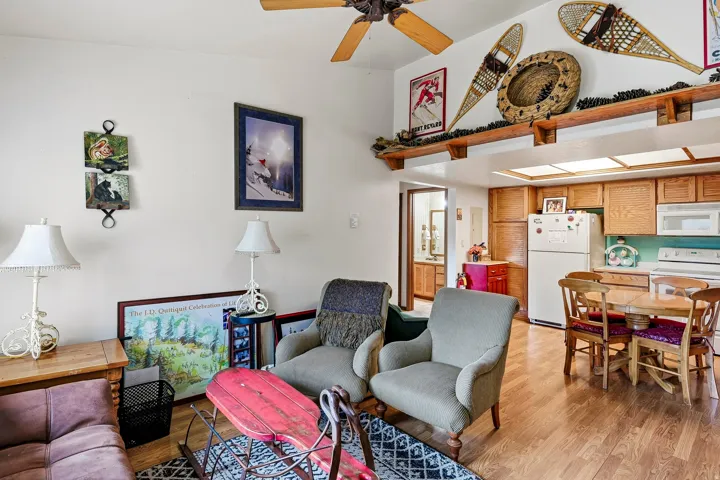 Vaulted ceiling with a ceiling fan, wood-finish flooring, wood cabinetry, built-in kitchen appliances, and an open dining area