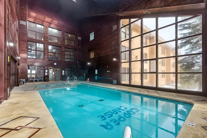 Indoor swimming pool with concrete decking, expansive multi-paned windows, and wood-paneled walls