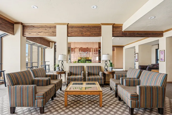 Recessed lighting illuminates a space featuring wood-finish ceiling beams, wood trim accents, and a patterned carpet