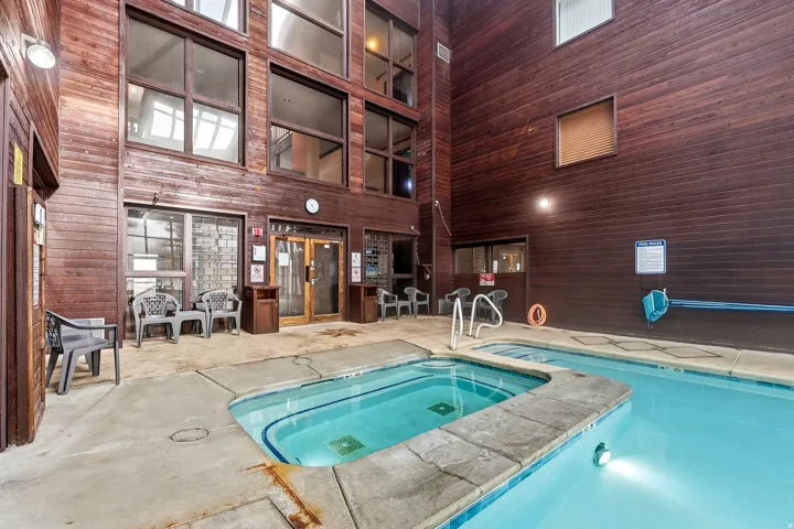 Indoor pool and hot tub with concrete surround and wood-paneled walls