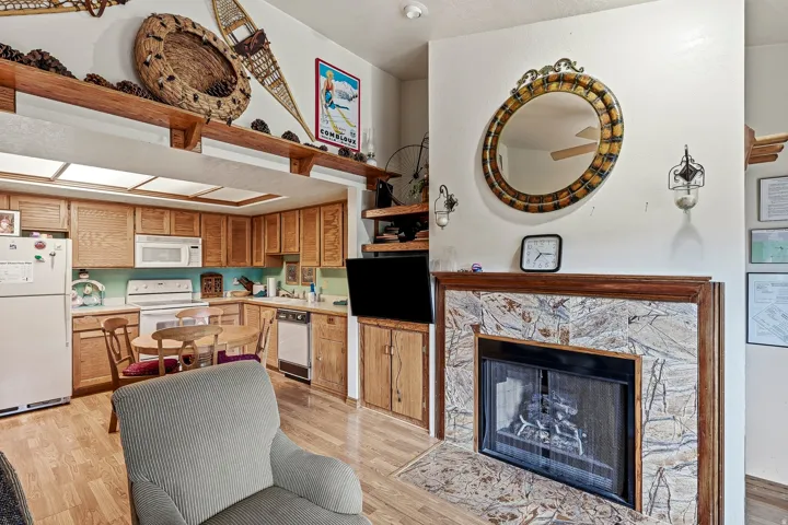 Open-concept living area featuring warm wood-finish flooring, custom wood cabinetry with ample storage, stainless steel appliances, and a gas fireplace with decorative stone surround