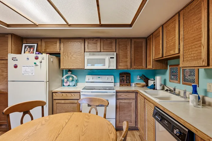 Wood cabinetry with louvered doors, white appliances, and a built-in microwave