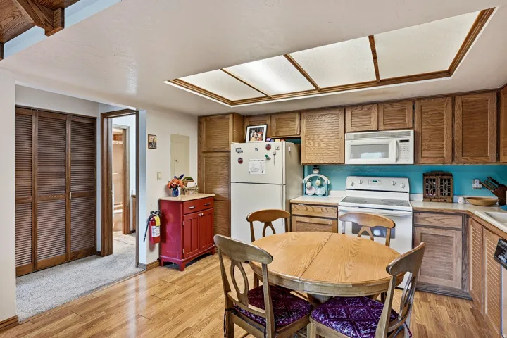Kitchen featuring wood-finish flooring, wood cabinetry, white appliances, and a fluorescent ceiling light fixture