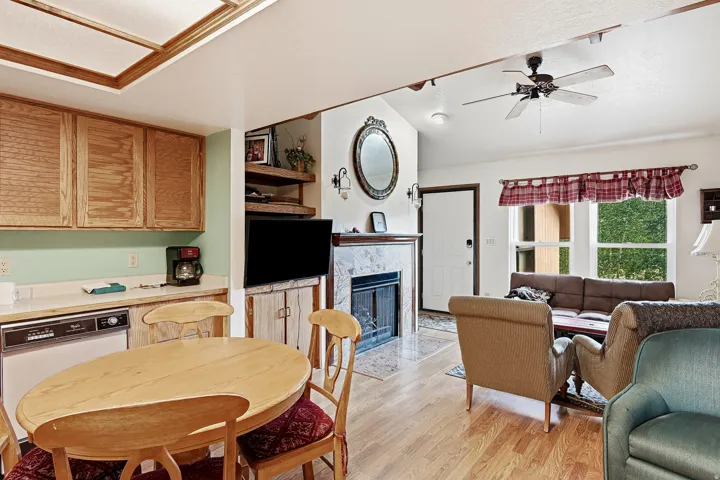 Hardwood flooring throughout, kitchen with wood cabinetry, fireplace with stone surround, vaulted ceiling, and ceiling fan
