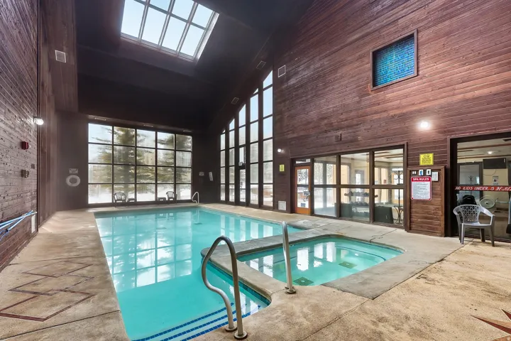 Indoor aquatic center featuring a resort-style heated swimming pool with spa jets, skylights flooding the space with natural light, wood-finish interior walls, large gridded windows, and direct access to adjacent facilities through glass doors