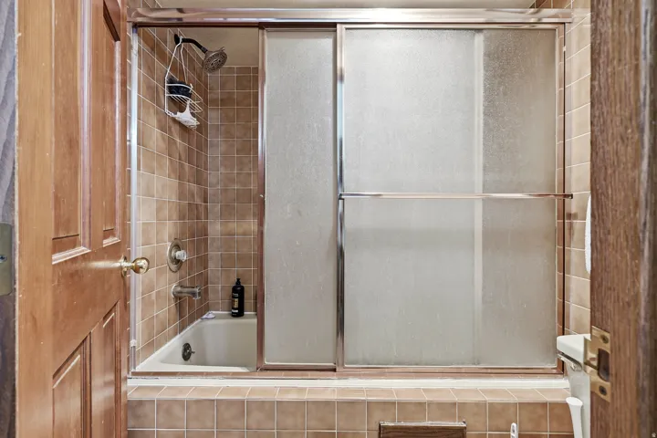 Updated bathroom featuring a tile-surround shower with glass sliding enclosure, chrome showerhead, and integrated shelf