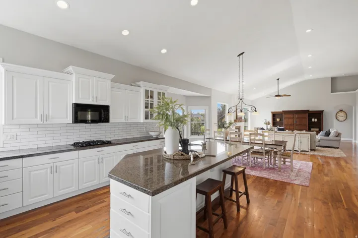 Vaulted ceilings, recessed lighting, wood-finish flooring, white cabinetry, and a kitchen island with stone-finish countertop