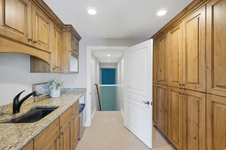 Galley kitchen featuring warm wood cabinetry with raised-panel doors, granite countertops, black undermount sink, stainless steel appliances, recessed ceiling lighting, and neutral tile flooring