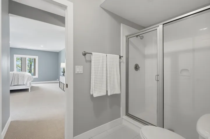 Modern primary bathroom featuring a frameless glass-enclosed shower with chrome fixtures, tile surround, and integrated showerhead