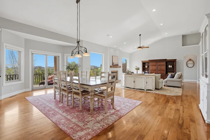 Bright open-concept dining and living area featuring hardwood flooring throughout, abundant natural light from multiple French doors and windows, a formal dining table with seating for eight, and a coffered ceiling with recessed lighting