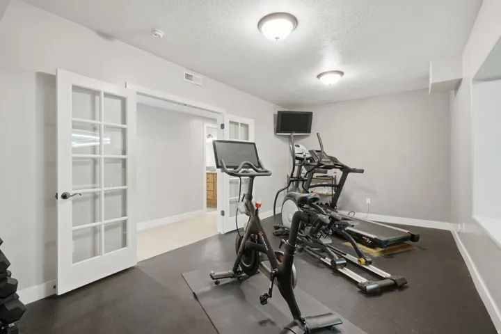 Dedicated fitness room featuring dark rubber flooring, recessed ceiling lighting, French doors with glass panels, and built-in wall space ideal for workout equipment and accessories