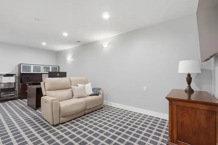 Finished basement recreation room featuring recessed ceiling lighting, geometric patterned flooring, built-in cabinetry with glass-front storage, wood-finish dresser, and neutral wall finishes ideal for versatile use