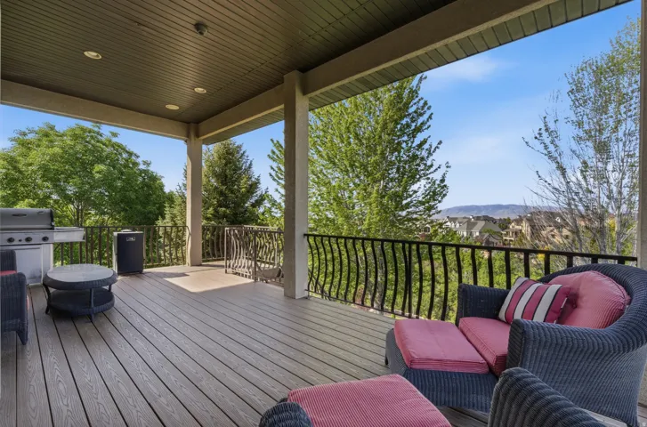 Expansive covered deck featuring composite wood-finish flooring, recessed lighting, and ornate metal railings