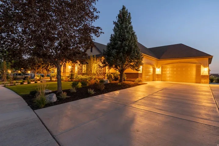 Two-car garage with arched entryways, exterior wall sconces, concrete driveway, stone accents, and mature landscaping