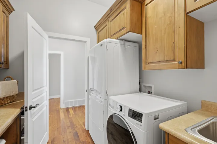 Dedicated laundry room featuring wood-finish cabinetry, stainless steel front-load washer and dryer, laminate countertops, and wood-finish flooring throughout