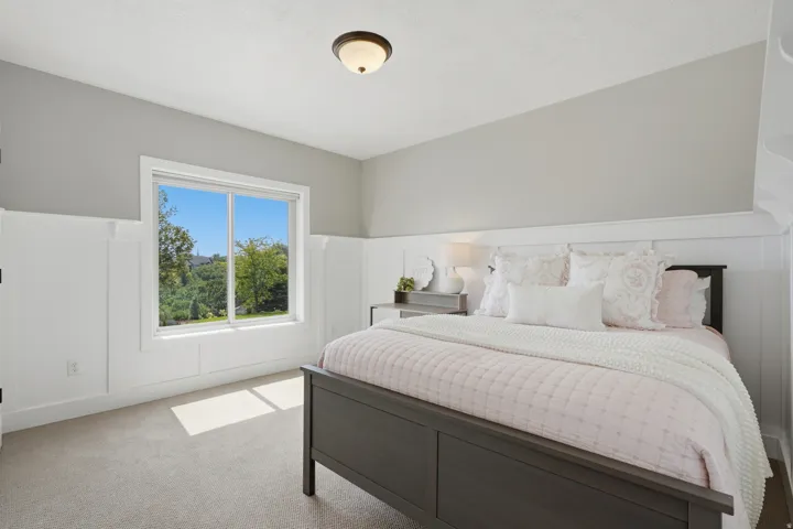 Bright secondary bedroom featuring white wainscoting, soft gray walls, and carpeted flooring