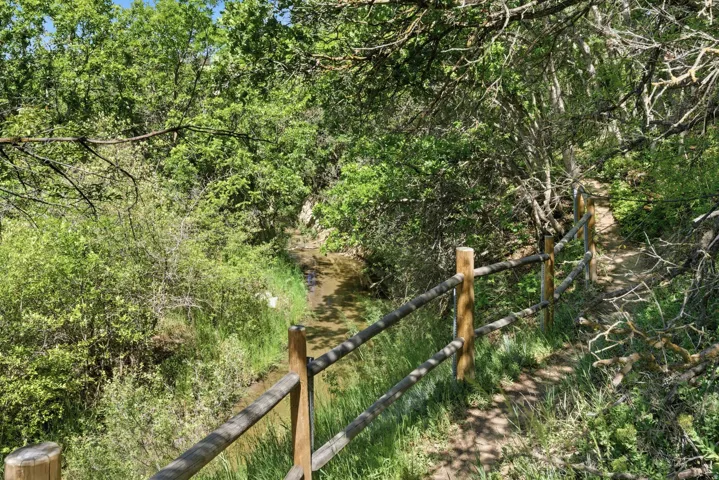 Scenic woodland trail featuring a rustic wood-rail fence, mature tree canopy, and natural stone pathway winding through lush vegetation and native landscaping