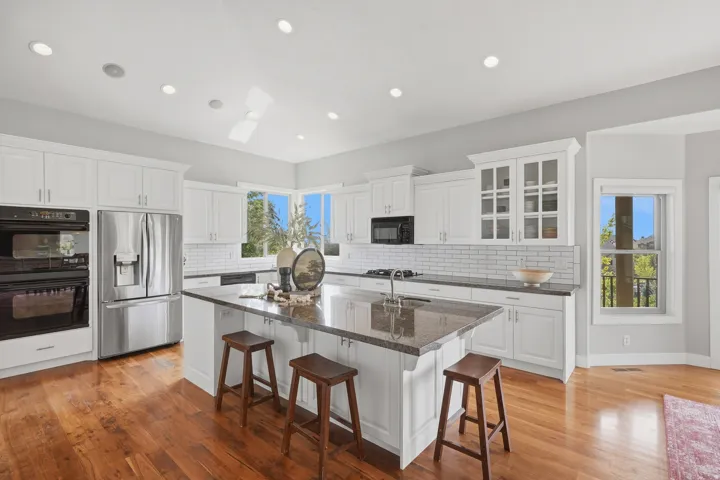 Kitchen featuring white shaker cabinetry, stainless steel appliances, a large center island with a stone-finish countertop, white subway tile backsplash, and wood-finish flooring