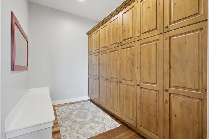 Spacious walk-in closet featuring extensive wood cabinetry with recessed panel doors, hardwood flooring, and neutral wall finishes