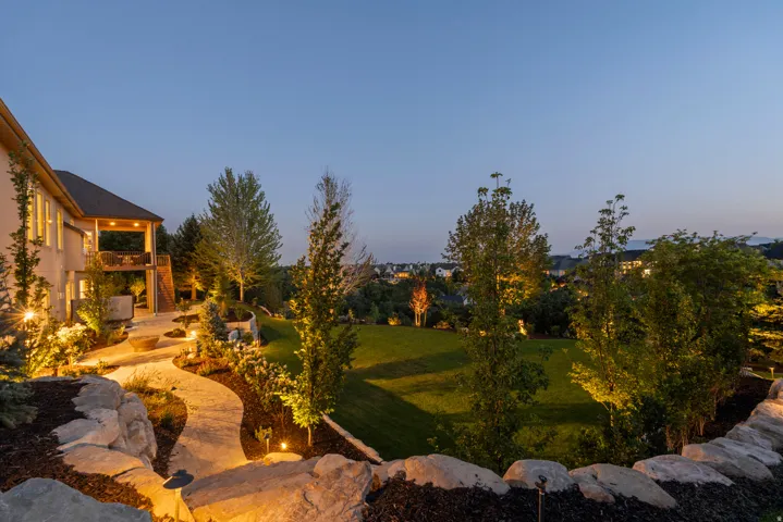 Expansive backyard oasis featuring manicured lawn, mature landscaping with columnar evergreens, and professional ambient lighting throughout