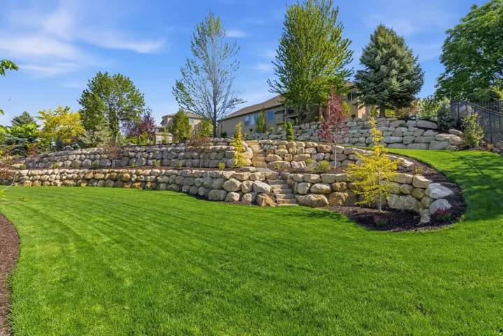 Expansive lawn with multiple tiered natural stone retaining walls, integrated stone steps, and varied mature landscaping