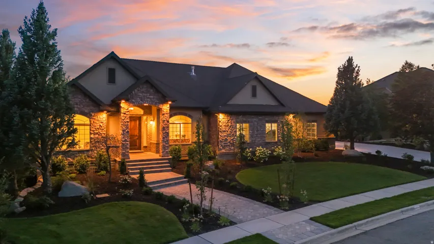 Stone and stucco exterior, arched windows, covered entryway, landscaped grounds with mature trees, paved walkway
