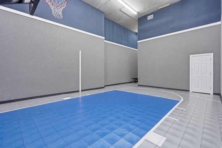 Indoor court featuring a basketball hoop, blue sport court flooring, and neutral-toned textured walls