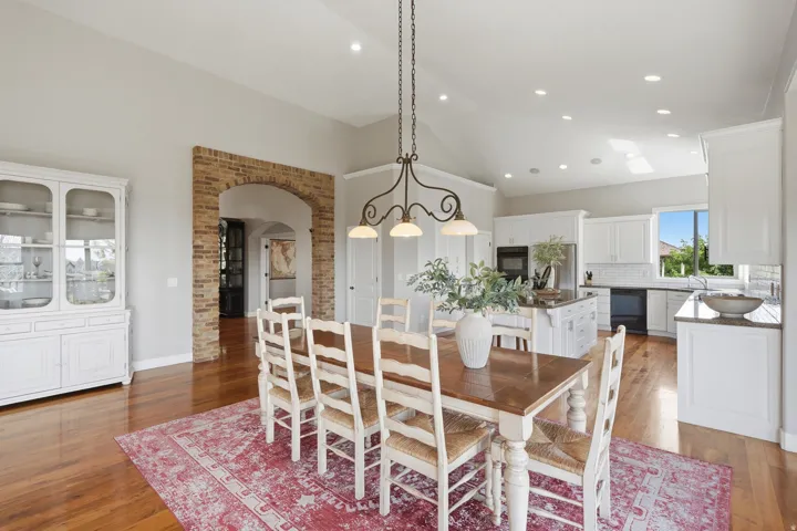 Hardwood flooring throughout, brick archway, vaulted ceilings, recessed lighting, and a kitchen featuring white cabinetry and an island
