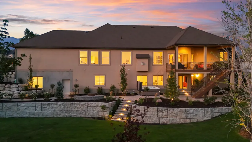 Modern home featuring a stucco exterior with dark architectural roofing, illuminated by landscape and architectural lighting