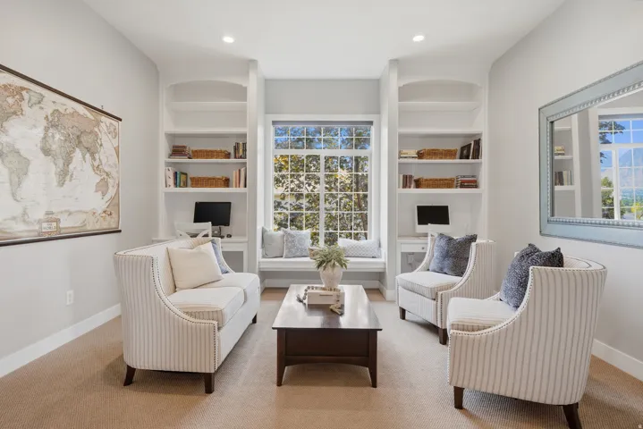 Sophisticated study featuring dual built-in shelving units with warm wood-finish accents, recessed ceiling lighting, and a large multi-pane window framed by arched alcoves