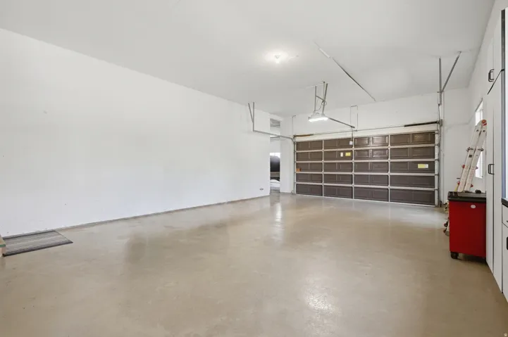 Spacious garage with polished concrete flooring, overhead storage shelving with multiple compartments, pendant lighting, and a dark-finish garage door