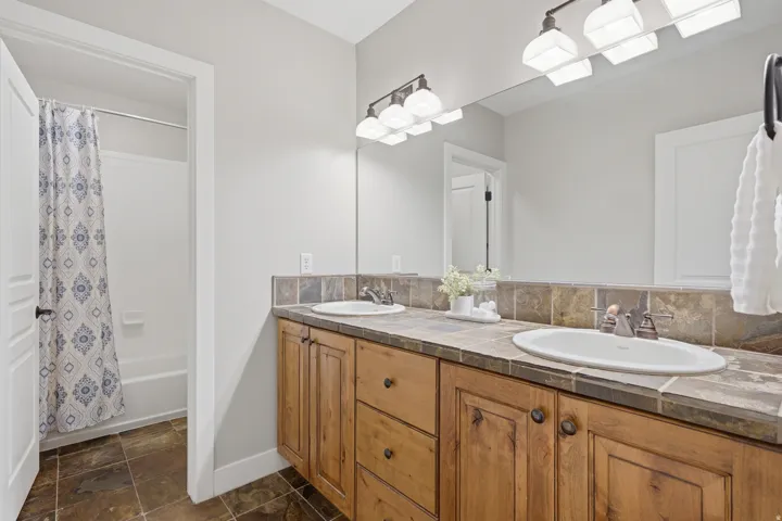 Spa-inspired master bathroom showcasing a wood-finish vanity with dual sinks, quartz countertop, and brushed nickel fixtures