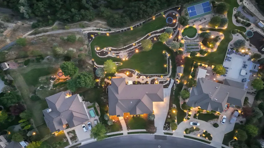 Aerial view showcasing an expansive estate with manicured grounds, mature landscaping, and professionally designed hardscaping throughout