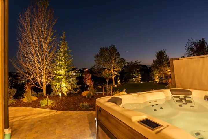 Patio with built-in spa, paver hardscaping, mature trees, landscaped planting beds, and outdoor accent lighting