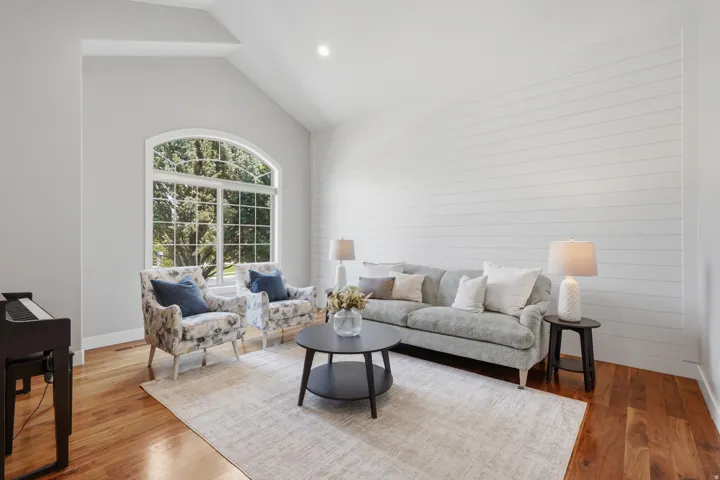 Bright, light-filled living room featuring soaring vaulted ceilings, arched transom windows with multiple panes, and white shiplap accent wall