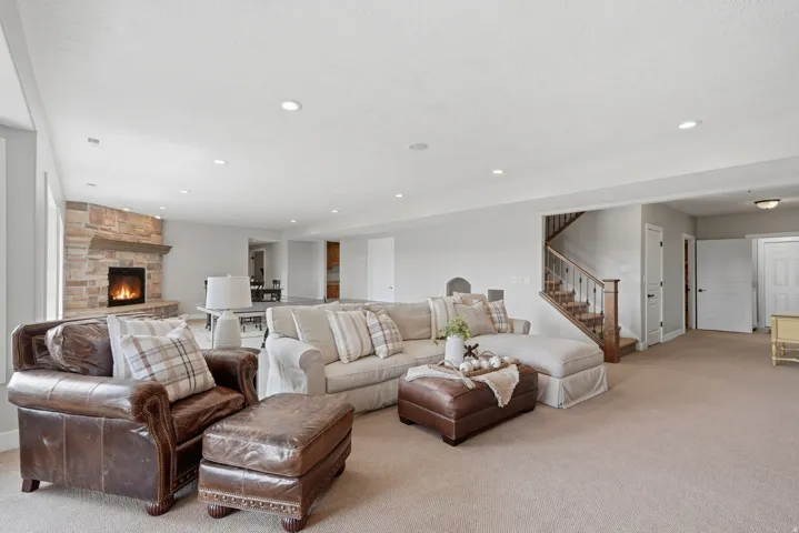 Stone-clad fireplace, built-in recessed lighting, wood staircase with dark metal spindles, and light-toned carpeting