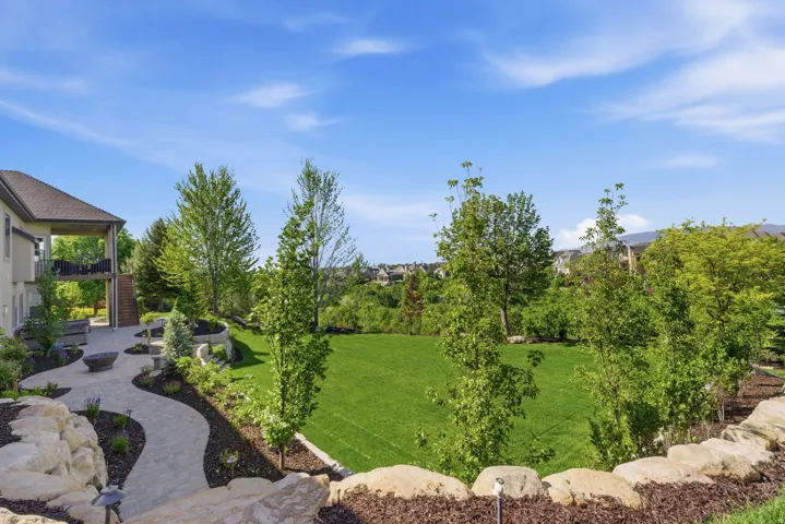 Expansive manicured lawn with mature landscaping and columnar evergreens, complemented by a curved stone hardscape and natural boulder edging