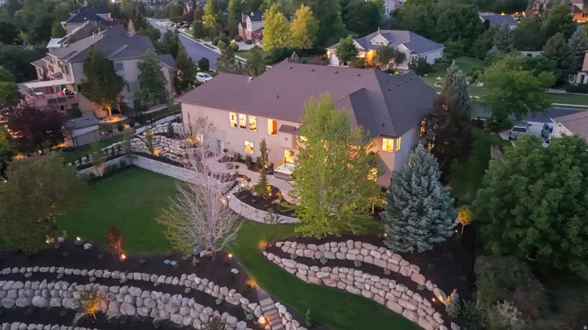 Elegant residence showcasing a spacious backyard with manicured lawn, mature landscaping including evergreen and deciduous trees, and curved stone hardscaping features