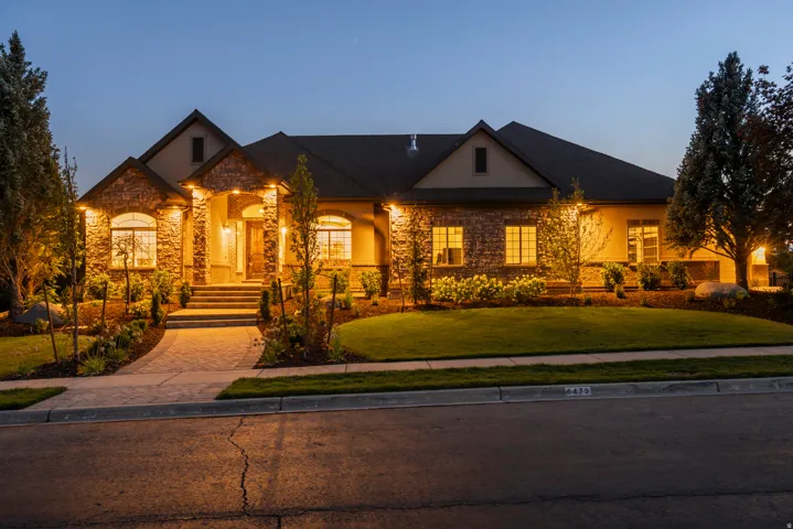 Elegant stone and brick exterior with dramatic uplighting, complemented by manicured landscaping and mature evergreen plantings