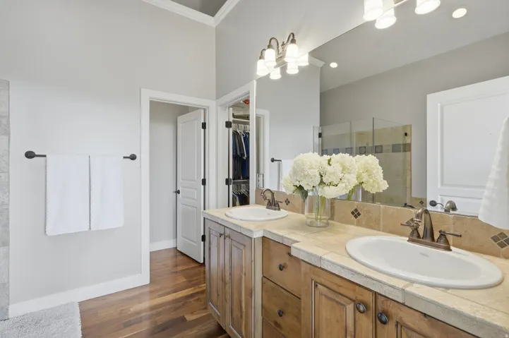 Spa-inspired primary bathroom featuring a wood-finish vanity with dual sinks, marble countertops, and brass fixtures