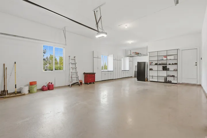 Spacious garage featuring multiple windows, abundant built-in cabinetry, overhead storage, and light-toned flooring