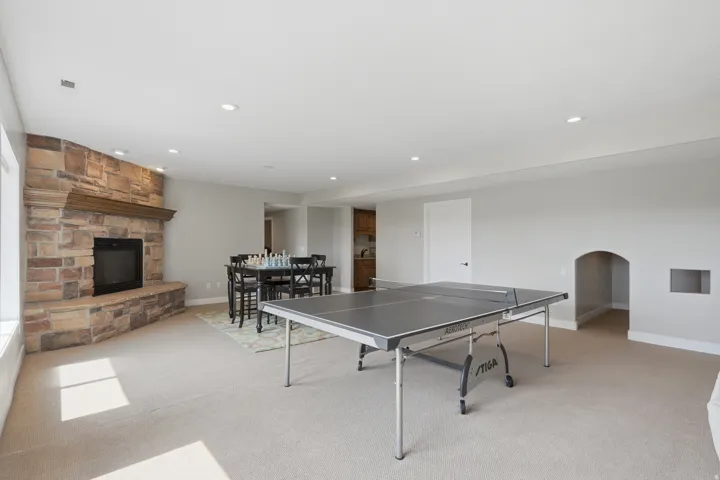 Spacious room with recessed lighting, stone fireplace with hearth and wood mantel, light-colored carpeting, and an arched wall niche
