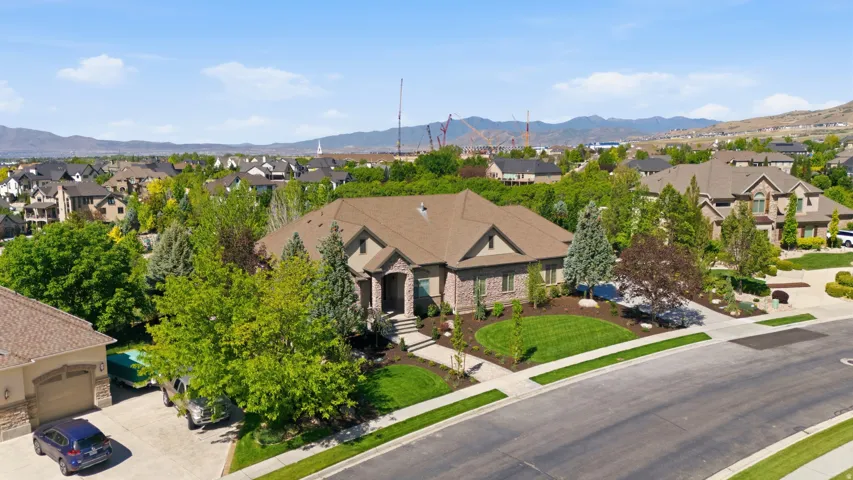 Elegant stone and stucco residence showcasing a covered front entry, mature landscaping with established trees framing the property, manicured lawn, and a circular driveway