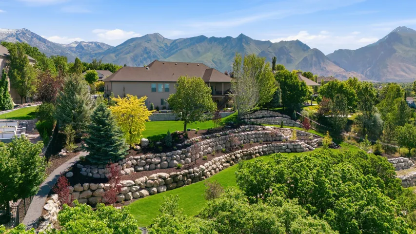 Expansive sloped yard featuring tiered stone retaining walls, manicured lawn, and mature trees